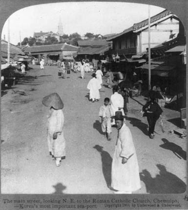 a large street with small buildings on each side. several people walk down the street