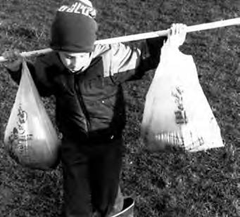 a kid carries a stick with bags on each side on his shoulders