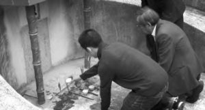 Two men bend down by a gravesite. 