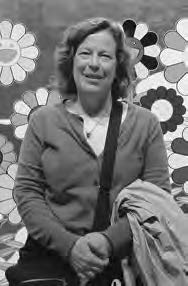 A middle-aged smiling woman standing in front of a Takashi Murakami rainbow sunflower mural. 