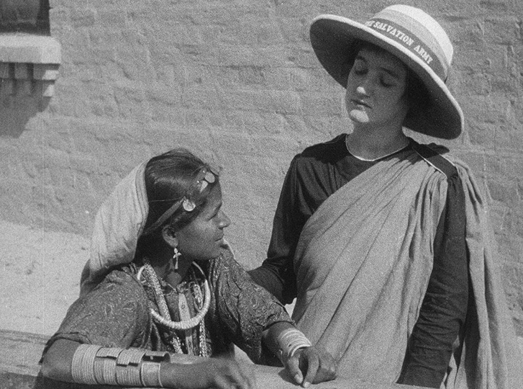 a woman wearing a salvation army hat touches the shoulder of an indian woman