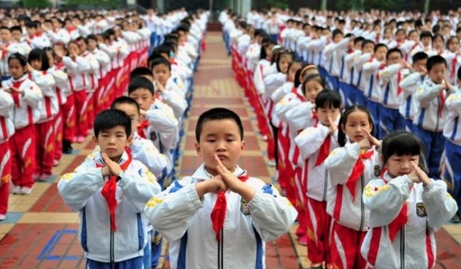 Hundreds of pupils are practicing martial arts. They are in line, all wearing red scarfs and uniforms. 