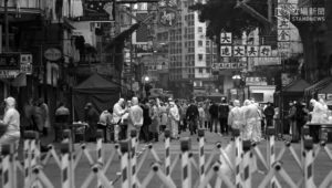 large lines of people wait to be tested by people in all white full body suits. there is quarantine fencing between these people and the viewer (you)