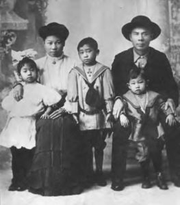 a black and white portrait of a family of five. Three children stand with their sitting mother and father.
