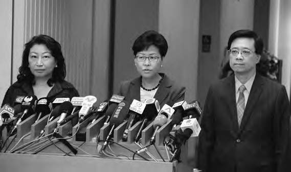 two women and a man in suits stand before many microphones