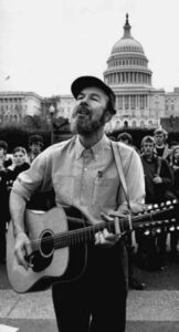 black and white photo of a man playing guitar and standing in front of the capitol building
