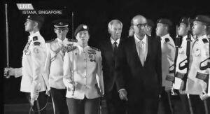 two men in suits walk by two lines of people in military uniforms