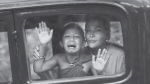 black and white photo of a girl crying and looking out a car window, as a woman holds her and smiles