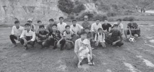 black and white photo of a group of young boys and their teacher at the front holding an infant