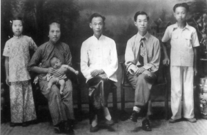 Two men and a woman were sitting in chairs holding a baby, and two children were standing on either side of them