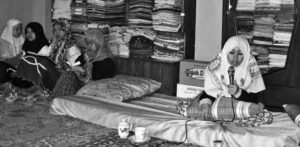 photo of several woman in hijab, they are sitting on the floor and on a mattress, with on singing into a microphone