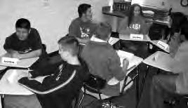 a photo of several teens sitting at desks, smiling and talking with each other