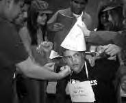 a photo of teens around one boy, placing a cap on his head
