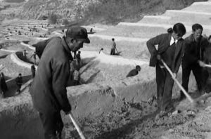 villagers work to shape the land beneath them with sticks. large plateaus can be seen behind them. 